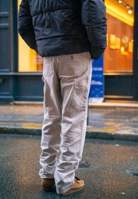 Pantalon cargo beige à coupe décontractée, avec poches latérales et écusson logo à l'arrière. Porté avec des chaussures marron.