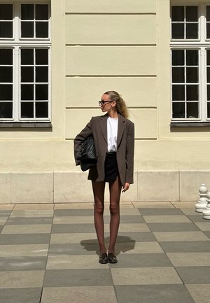 Rudas perdidžiaus švarkas ant baltos marškinių, derinamas su juoda mini sijonu ir juodais batais. Pridėtas pintas juodas rankinukas. Kvadratiniai plytelių fono.