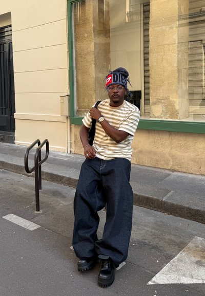 Pantalones de mezclilla oscuros de gran tamaño combinados con una camiseta de rayas color crema. Unos zapatos de plataforma negros y un gorro multicolor completan el look.