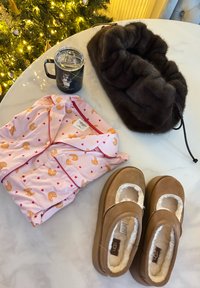 Ensemble de pyjama rose avec motifs de croissants et de cœurs, une tasse isolante noire, un serre-tête en fausse fourrure marron foncé, et des chaussons beige avec doublure crème.