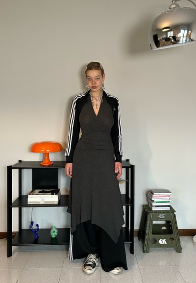 Chaqueta con cremallera a rayas en blanco y negro sobre un vestido gris con dobladillo asimétrico, combinada con pantalones anchos negros y zapatillas.