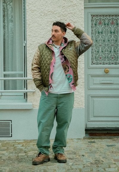 Chaqueta acolchada verde oliva y beige sobre una sudadera rosa con patrones circulares, camiseta blanca, pantalones verde claro y zapatos con estampado de leopardo.