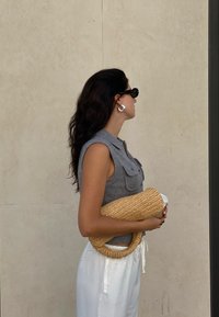 Grå strikket ærmeløs top med krave og lommer, hvide vide bukser og en struktureret stråhåndtaske. Mørke solbriller og ringeøreringe.