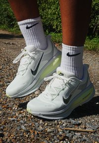 Bele tene patike Nike za trčanje s teksturiranim mrežastim gornjim dijelom, crnim Swoosh logom i svijetložutom detaljem od jastučića. Nosi se s bijelim čarapama do gležnja.