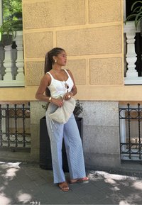 White tank top with a front tie, pinstriped wide-leg trousers, beige fabric bag with drawstrings, and brown sandals against a street backdrop.