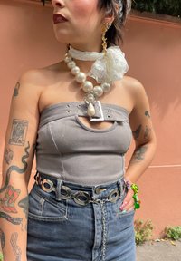 Γκρι strapless τοπ με λεπτομέρειες από οπές, ψηλόμεσα μπλε τζιν, ασημένια ζώνη αλυσίδας, υπερμεγέθη κολιέ από πέρλες και δαντελένιες λεπτομέρειες.