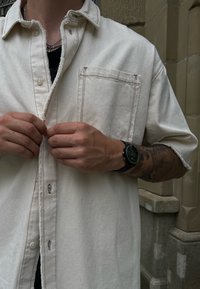Balta džinsinė palaidinė su kišene, pasižyminti kontrastingais raudonais siūlais. Palaidinė yra laisvo kirpimo ir turi sagčių apykaklę.