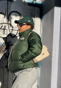 Πράσινο τζάκετ πούφ με ψηλό γιακά, οριζόντιες ραφές, συνδυασμένο με ριγέ παντελόνια και μπεζ τσάντα χιαστί. Μαύρα γυαλιά ηλίου.