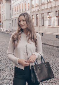 Svetlosivý kardigán na gombíky, nosený cez svetlý top. Čierna kabelka obdĺžnikového tvaru s dvoma rukoväťami. Pozadie z dláždenej ulice.