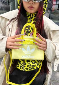 Rumena prozorna torba z kratkimi ročaji, ki ima bel Adidasov logotip, dopolnjena z živopisno jakno z živalskim vzorcem in pisanimi nohti.