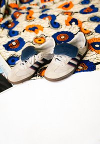 Vita och grå mockaskor med blå accenter och randiga detaljer, med en texturerad, vadderad tunga och bruna gummisulor.