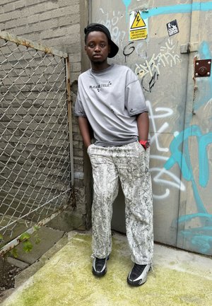 Camiseta de gran tamaño color gris claro con texto negro, pantalones con estampado de serpiente en tonos de gris y blanco, y zapatillas negras con acentos plateados.