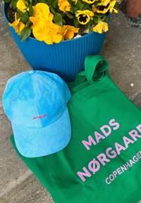 Šviesiai mėlynas kordūrovinis kepuraitė su raudonai siuvinėtu žodžiu "AMOUR", šalia žalia pintinė rankinė su rožinėmis raidėmis "MADS NØRGAARD COPENHAGEN".