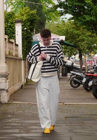Gestreepte trui met een rits, wit en marineblauw; losse witte broek; gele sneakers; draagt een crèmekleurige schoudertas met zwarte hengsels.