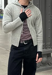 Ljusgrå zip-up hoodie med ribbade ärmslut och nederkant, bärs över en mörk t-shirt. Svarta byxor och ett tunt svart bälte med silverdetaljer.