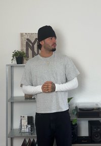 Hall grey lühikeste varrukatega särk valge pika varrukaga särgi peal, kombineeritud tumedate teksadega. Must beanie, kätele nähtavad tätoveeringud.