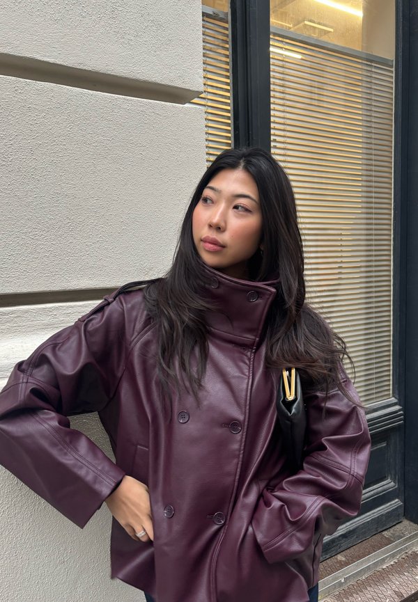 Giacca in pelle bordeaux con collo alto e design doppiopetto, con grandi bottoni e vestibilità comoda. Texture liscia e maniche lunghe.