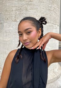 Zwarte mouwloze top met een vloeiende halslijn, gevlochten haar in twee secties gestyled, en een glanzende make-up met roze blush en lavendel lipkleur.