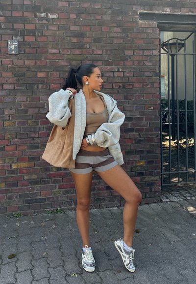 Sudadera gris de gran tamaño, camiseta sin mangas de color marrón claro, pantalones cortos a rayas y zapatillas plateadas. Textura suave, corte casual, hardware mínimo y colores neutros.