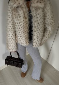 Veste en fausse fourrure à motif tacheté, pantalon de jogging gris, bottines marron et petit sac à main sombre avec détails noués.