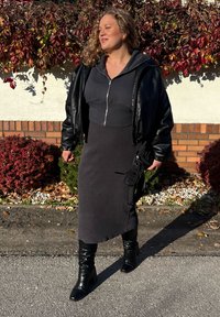 Giacca bomber in pelle nera sopra una felpa con zip grigio scuro e un vestito midi a coste. Stivali neri con tacco al ginocchio, con una finitura testurizzata.