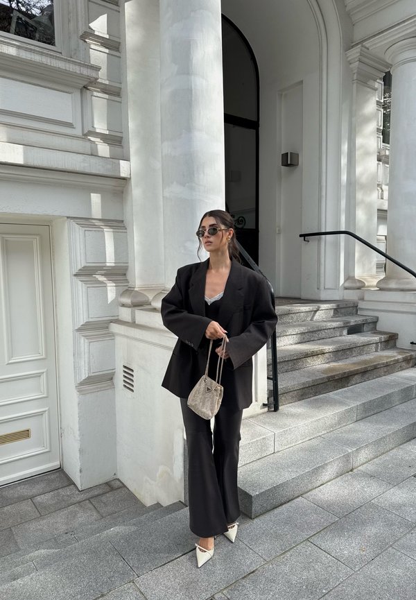 Black oversized blazer over a black top, teamed with flared trousers and white pointed-toe heels. Accessorised with a small woven bag and sunglasses.