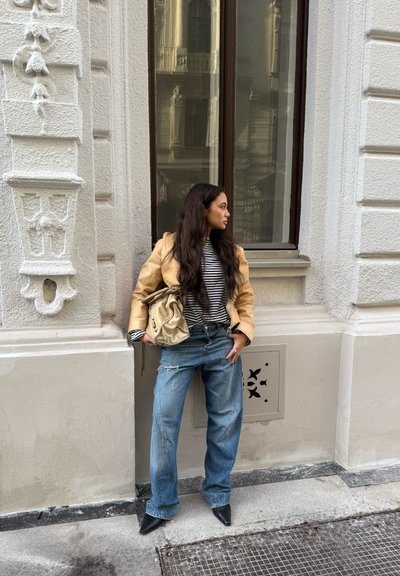 Blazer color canela sobre una camiseta a rayas blancas y negras, combinado con jeans de pierna ancha azules y tacones negros de punta afilada. Bolso beige colgado sobre el hombro.