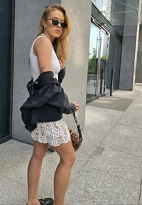 Μαύρο τζάκετ τζιν, λευκό λεπτό μπλουζάκι και λευκή μίνι φούστα με δαντέλα. Τα αξεσουάρ περιλαμβάνουν μαύρα γυαλιά ηλίου και τσάντα σε λεοπάρ σχέδιο. Λείος υφασμάτινος χαρακτήρας, σύγχρονος σχεδιασμός.