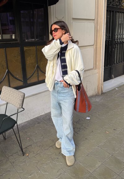 Chaqueta inflable blanca, bufanda a rayas azul marino, camiseta blanca, jeans de pierna ancha azul claro, zuecos de ante marrón claro y un bolso marrón con tachuelas metálicas.