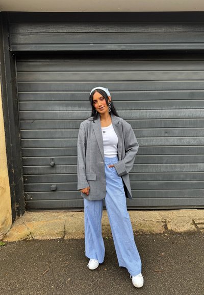 Blazer gris de gran tamaño, top blanco y pantalones anchos de rayas azul claro. Los accesorios incluyen una diadema y grandes pendientes. Zapatillas blancas.