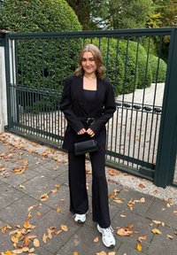 Černé na míru šité sako s pásem, kombinované s černým topem a širokými černými kalhotami. Bílé sportovní tenisky a malá černá kabelka.