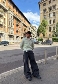 Ljusgrön tröja, svarta vida byxor, svarta stövlar; urban gatuvy med klassisk arkitektur och en klarblå himmel i bakgrunden.