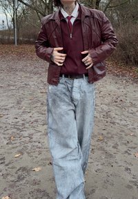 Maglione con zip color marrone scuro sotto una giacca di pelle marrone, abbinato a pantaloni larghi color azzurro chiaro. Presenta una vestibilità comoda e cuciture visibili.