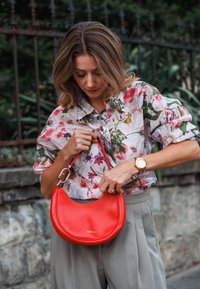 Crvena kožna torba s zakrivljenim oblikom i zlatnim dodacima, s imenom brenda "FURLA" utisnutim na prednjem dijelu.