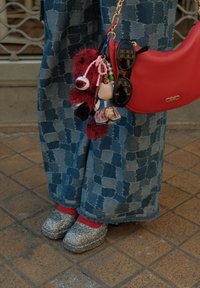 Röd handväska med guld detaljer, ihopparad med silverglittriga skor, blå rutiga vida byxor och röda strumpor. Nyckelringar som accessoarer är fästa.
