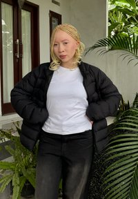 Juodas pūkinis švarkas su siuvinėjimu, dėvimas ant baltos marškinėlių, derinamas su juodomis kelnėmis. Fone matomi žali augalai.