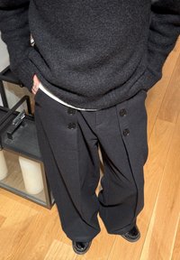 Maglione in lana nera con finitura testurizzata, abbinato a pantaloni neri a gamba larga con due grandi bottoni e una vestibilità comoda.