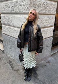 Czarna skórzana kurtka bomberka, dopasowany czarny golf, teksturowana miętowa spódnica z trójwymiarowymi szczytami, czarne kozaki za kolano, mała czarna torebka.