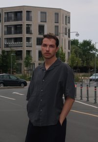 Koszula z krótkim rękawem, zapinana na guziki, w ciemnoszarym kolorze z bawełny, luźny krój z kołnierzem typu notch, zestawiona z luźnymi ciemnymi spodniami w miejski scenerii.