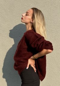Suéter de malha burgundy com um corte solto e ombros caídos, combinado com calças justas pretas. Textura suave e aparência suave.