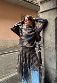 Strikket sweater i camouflage mønster, brune og grå toner; asymmetrisk ternet nederdel; blå jeans; lille brun håndtaske; lilla solbriller.