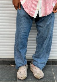 Calças de ganga azul claro com corte descontraído, combinadas com sapatos tipo slip-on bege texturizados com desenhos recortados. Camisa com padrão rosa e branco por cima.