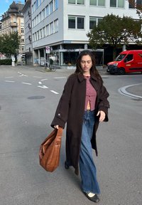 Pruun villane mantel, punaste ja valgete triipudega lühike top, lehvikujulised teksapüksid, kandmas pruuni nahast kotti, kõndimas linna tänaval.