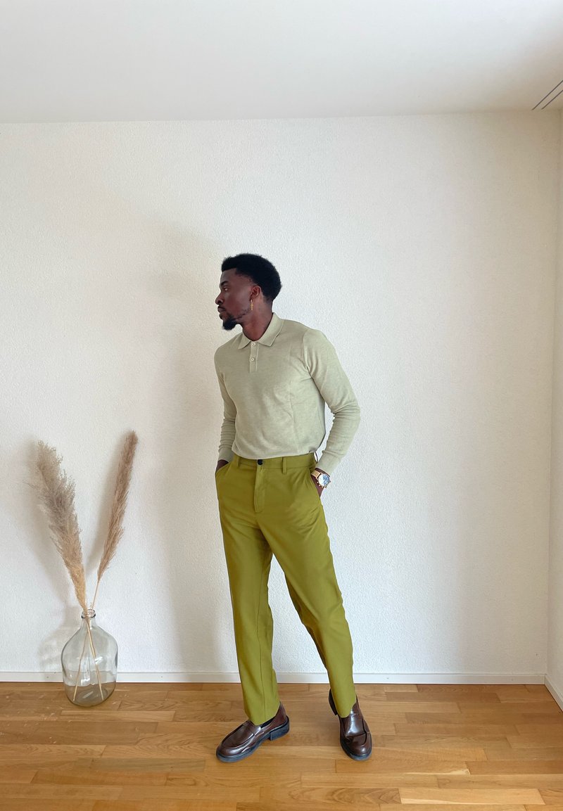 Polo-shirt à manches longues vert clair associé à un pantalon taille haute vert olive et des chaussures marron foncé, sur un fond neutre.