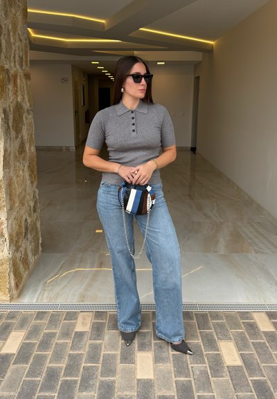 Camiseta polo de manga corta gris con canalé y botones, jeans de pierna ancha azules, tacones negros de punta afilada y un pequeño bolso multicolor con cadena.