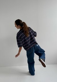 T-shirt rayé noir avec des lignes roses, coupe décontractée, associé à un jean en denim bleu ample et des baskets noires avec des accents blancs.