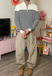 Maglione a righe con mezza cerniera in blu navy e bianco, abbinato a pantaloni larghi beige chiaro e stivali color cuoio. Design e tessuto semplici.