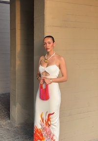 Vestido blanco con un diseño de cortes y un patrón de coral en el dobladillo. El accesorio incluye un bolso de cuentas multicolores. Textura suave.