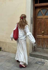 Fehér, csipkés felső puff ujjaival és csuklónál megkötőkkel; azonos hosszú szoknya bonyolult csipke mintával; piros válltáska; bordó lapos cipők.