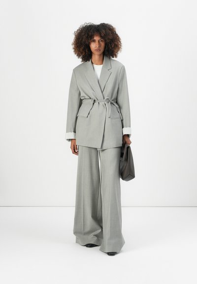 Blazer entallado gris claro con pantalones de pierna ancha a juego. El blazer cuenta con una cintura ceñida con cinturón y puños de manga acanalados. Textura de tela suave.